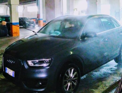 Autolavaggio self-service: Un uomo lava un'Audi Q3 grigia in un garage con idropulitrice ad alta pressione, servizio di pulizia auto.