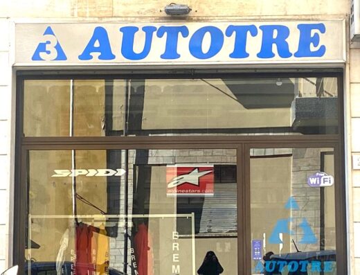 Vetrine del negozio Autotre Arezzo, rivenditore di abbigliamento e accessori moto, con marchi Spidi, Alpinestars e Brembo visibili.