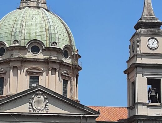 Architettura barocca con cupola verde e campanile con orologio a Baaria House Hotel, Sicilia. Cielo azzurro sullo sfondo.