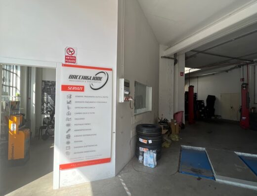 Ingresso dell'officina Bacchiglione Meccanica & Pneumatici, con cartello servizi, pneumatici impilati e attrezzatura per riparazioni auto e moto.