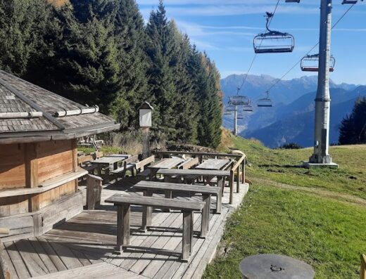 Baita Goles mountain restaurant with Guinness sign, wooden tables, and ski lift in the background, offering a scenic view for motorcycle travelers and visitors.