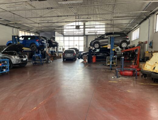 Interno di Balilla C R M – Centro Revisioni e Autofficina con auto su elevatori, meccanico al lavoro e attrezzature per la manutenzione veicolare.