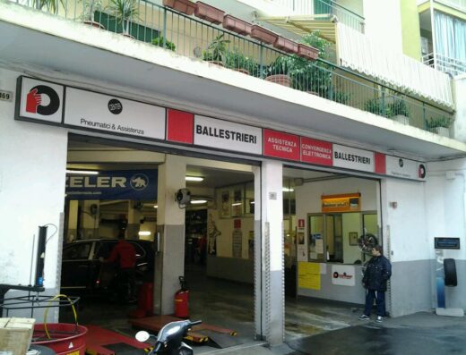 Foto dell'officina Ballestrieri Sas Di Ballestrieri Leo E C. con insegne "Pneumatici & Assistenza", auto in riparazione e moto parcheggiata. Servizi di assistenza tecnica e convergenza elettronica.
