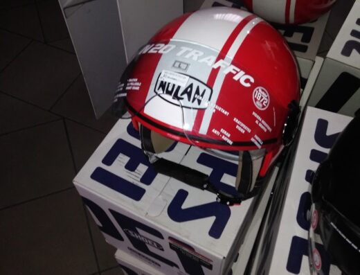 Caschi da moto Nolan e Major rossi e bianchi impilati su scatole, accessori e abbigliamento per motociclisti Bartollini Moto