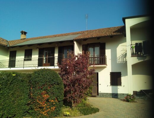 B&B Bertaina Mauro: Facciata di un edificio a due piani con balconi, circondato da vegetazione e pavimentazione in pietra.