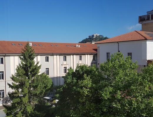 Vista dalla finestra di B&B Casa Angela, con edifici storici e alberi rigogliosi, sotto un cielo azzurro.