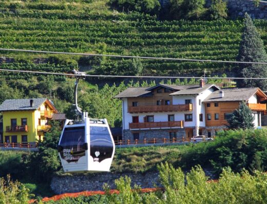 Telecabina Pila Ski a Gressan, Valle d'Aosta, con vista panoramica sulle case tipiche e i vigneti. Servizi di trasporto e turismo in montagna.