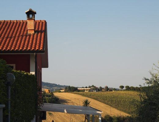 Vista panoramica di una casa di campagna con tetto in tegole rosse, circondata da campi coltivati, ideale per un soggiorno rilassante in un b&b.