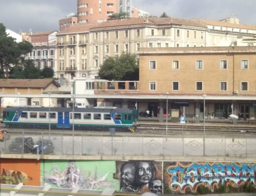 View of Campobasso train station in Italy with a regional train pulling into the platform, buildings and graffiti in the foreground.