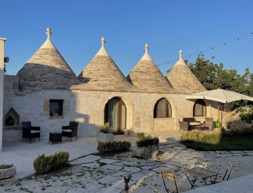 B&B in Masseria Agli Antichi Trulli: Esterno di una masseria con trulli, sedie e tavoli in pietra, tipica architettura pugliese per un soggiorno indimenticabile.