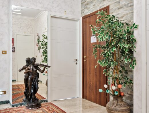 Interno del B&B In Riva al Lago con scultura di donna che suona il violino riflessa in uno specchio, porte di camere e pianta decorativa.