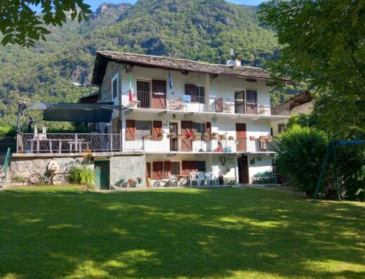 B&B La Ghita: A charming two-story bed and breakfast nestled in the Italian Alps, featuring balconies, a lush green lawn, and mountain views.