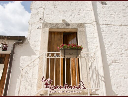 Ingresso del B&B La Lanterna, con porta in legno, balcone fiorito e insegna, ideale per viaggiatori e motociclisti in cerca di alloggio.