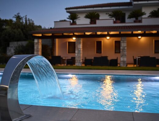 Immagine di una piscina illuminata di sera presso B&B Le Bianche, con cascata d'acqua e l'edificio sullo sfondo.
