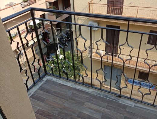 Vista dal balcone del B&B Omnia Scilla, con ringhiera in ferro battuto e scorcio su una strada dove è parcheggiata una moto.