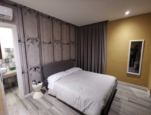 Camera da letto arredata con letto matrimoniale, comodino di design, bagno in camera e specchio a figura intera, ideale per un soggiorno confortevole in un B&B.