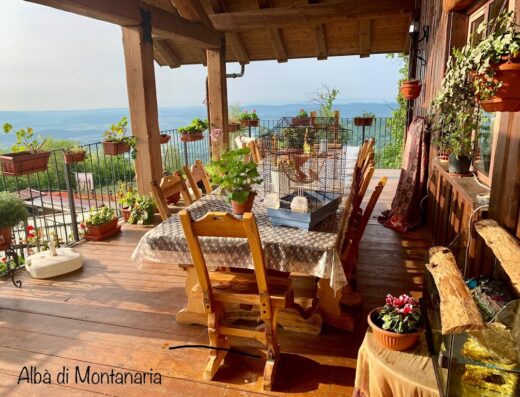 Outdoor dining area at B&B Ranch Alba Montanaria in Valchiusella, Italy, featuring a wooden table and chairs, potted plants, and scenic mountain views, perfect for a relaxing vacation near horse riding trails.