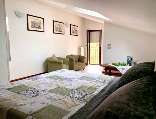 Interno di B&B Sguardo al Conero: letto matrimoniale con copriletto patchwork, poltrone verdi, tavolo con servizio da tè e balcone con vista.