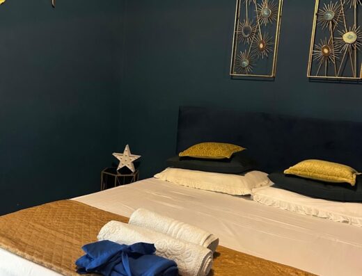 Camera da letto con letto matrimoniale, cuscini decorativi dorati, asciugamani arrotolati e decorazioni murali in stile moderno al B&b Terrazza Filangiò.