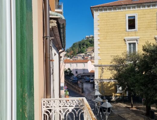 Vista dal balcone di B&B Terrazza Flora, con ringhiera in ferro battuto, strada con auto e architettura storica. Ideale per viaggi e turismo.