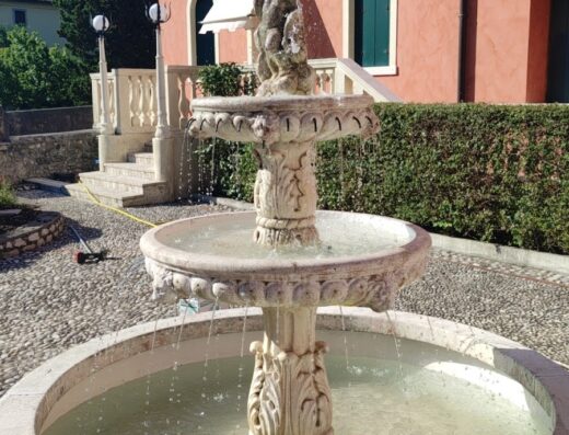 Fontana decorativa in pietra a B&B Villa Carli, con acqua zampillante e edificio rosa sullo sfondo, atmosfera rilassante e accogliente.