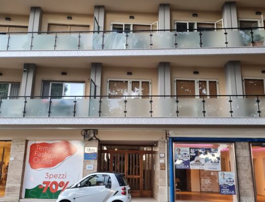 Una Smart bianca parcheggiata di fronte a un edificio a più piani con balconi e negozi al piano terra, in Italia.