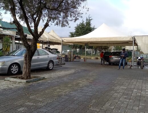 Auto di lusso in un autolavaggio con personale che esegue la pulizia professionale, sotto una tettoia e con pavimentazione in pietra.