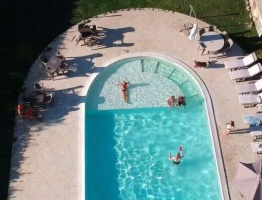 Vista aerea di una piscina presso il Bed & Breakfast Case Osti, con persone che nuotano e prendono il sole, circondata da lettini e tavoli.