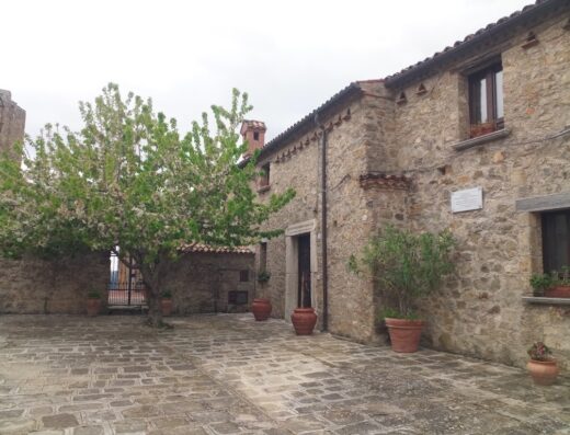 Bed & Breakfast del Corso: Scorcio esterno di un edificio in pietra con albero fiorito e pavimentazione in pietra, atmosfera accogliente.