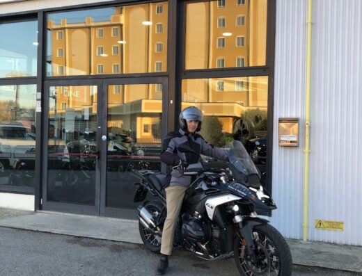 Un motociclista in posa davanti a Bellan & Giardina BMW con una BMW R 1250 GS Adventure nera, ideale per viaggi e avventure.