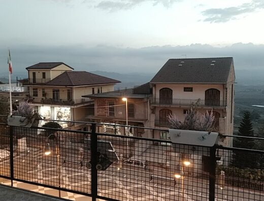 Veduta panoramica di Belvedere, Italia, con edifici illuminati, bandiera italiana e montagne sullo sfondo, ideale per viaggi in moto e scoperta del territorio