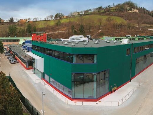 Vista esterna dello stabilimento Benelli Armi S.P.A., produttore italiano di motociclette e armi da fuoco, con parcheggio auto e area verde circostante.