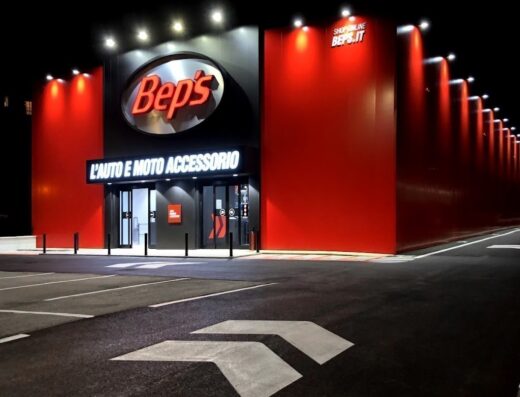 Foto notturna del negozio Bep's di Alessandria, forniture per auto e moto, illuminato con insegna 'L'auto e moto accessorio' e parcheggio.