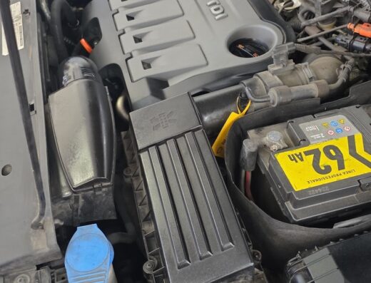 Dettaglio del motore di un'auto Volkswagen TDI in riparazione presso BeshoGarage, con batteria, filtro dell'aria e altri componenti visibili.