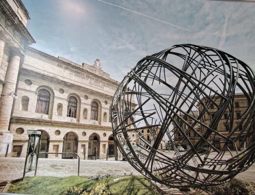 Scultura sferica in metallo presso l'Hotel Best Western I Colli a Macerata, Italia, con edificio storico sullo sfondo.