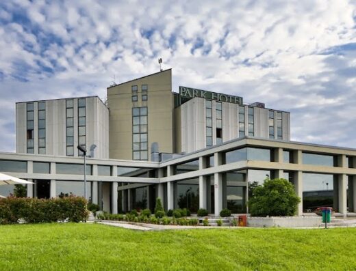 Vista esterna del Best Western Park Hotel con prato verde curato, ombrelloni bianchi e cielo nuvoloso.