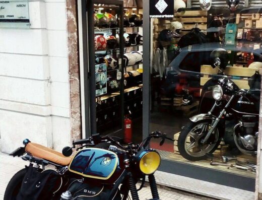 Motocicletta BMW customizzata parcheggiata di fronte al negozio BHM, specializzato in abbigliamento e accessori moto. In vetrina caschi e un'altra moto Honda.