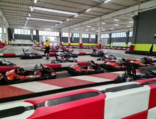 BI Karting s.n.c.: Pista interna con go-kart pronti per la corsa, piloti con caschi e personale di servizio con bandiera gialla.