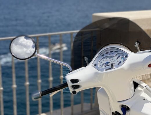 Dettaglio di una Vespa bianca di Bianca Rent a Polignano a Mare con vista mare. Scooter ideale per esplorare la costa pugliese.