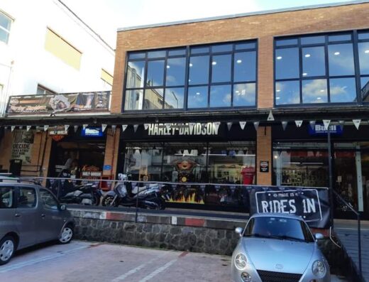 Big On The Road Napoli: Harley-Davidson dealership exterior with motorcycles, accessories, and service bays visible. Two cars are parked in front.