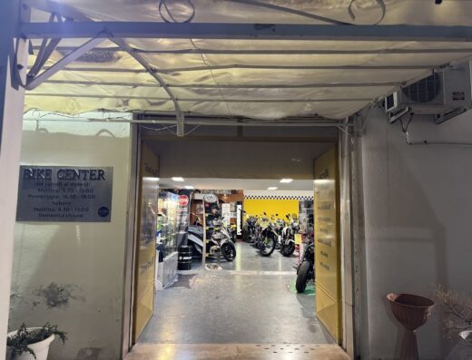 Ingresso del Bike Center, negozio di moto e accessori. Si vedono diverse moto all'interno e l'insegna con gli orari di apertura.