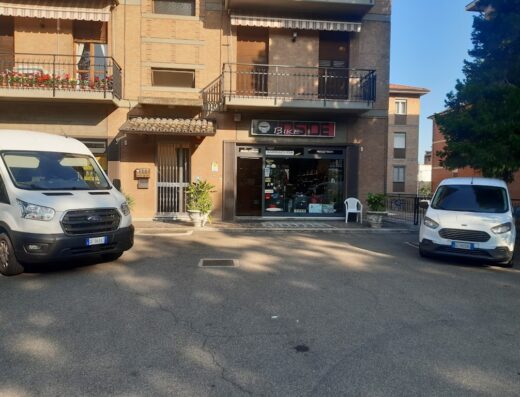 Bike Inside store front in Reggio Emilia, Italy, featuring motorcycles and accessories with two white service vans parked nearby.