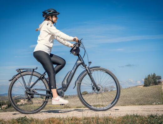 Una ciclista con casco partecipa a un tour in bici a Firenze, pedalando su una e-bike su una strada di campagna con vigneti sullo sfondo.
