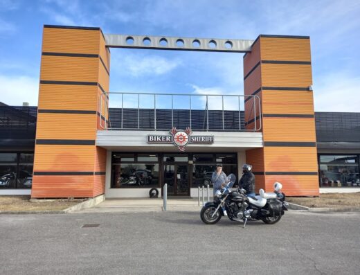 Un motociclista di fronte al negozio Biker Sheriff con la sua moto. Negozio di accessori e abbigliamento per motociclisti.