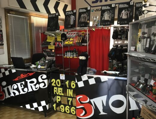 Interno del negozio Bikers Store a Piacenza, con esposizione di abbigliamento e accessori moto, caschi, guanti e protezioni. Presente il bancone con il logo del negozio.
