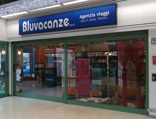 Bluvacanze Bologna C.C. Via Larga travel agency storefront with blue sign, glass doors, and promotional travel materials visible inside.