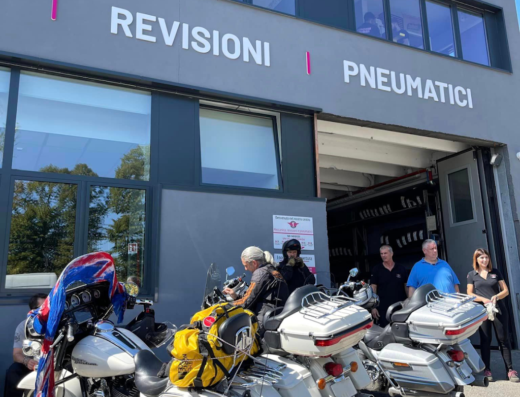 Motociclette Harley-Davidson di fronte a Bologna Gomme per revisioni e pneumatici, con motociclisti e personale dell'officina visibili.