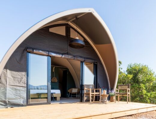 Borgo di Campagna Glamping tent with open sliding glass doors revealing a bed, seating, and outdoor wooden deck with chairs.