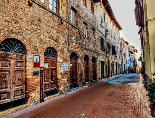 Strada acciottolata a Borgo La Casaccia, Italia, con edifici in mattoni, porte ad arco in legno e segnaletica turistica che indica area Wi-Fi gratuita.