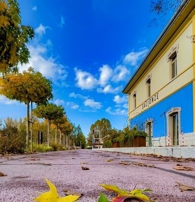 Borgo Stazione Bike Inn in Italia: vista esterna dell'edificio con cielo azzurro e foglie autunnali sul sentiero, ideale per cicloturismo e viaggi in moto.
